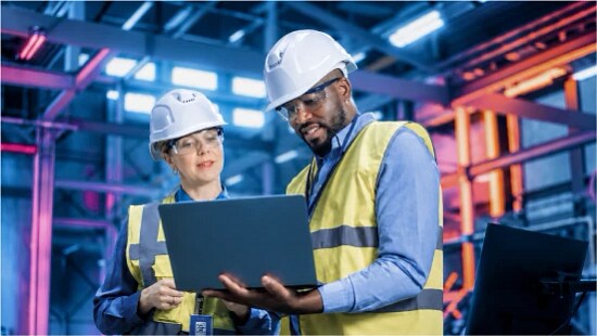 two workers in an industrial plant looking at a laptop
